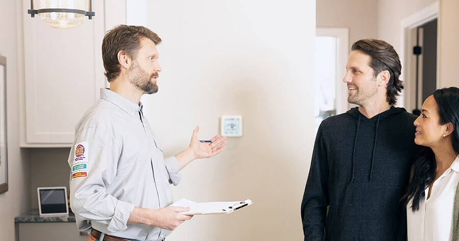 An installer is teaching the homeowner how to set up the smart thermostat on the wall.